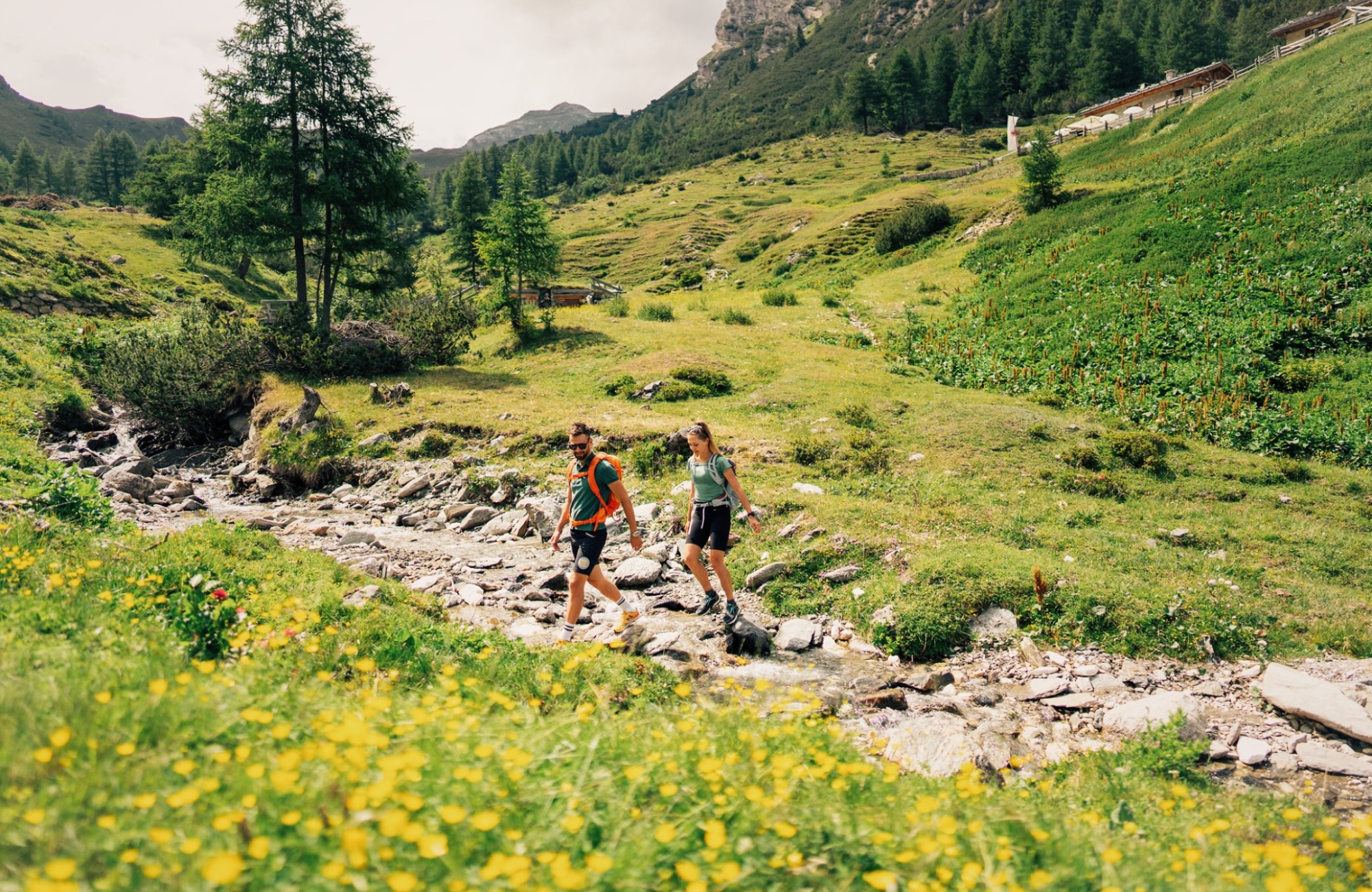 A couple crosses the stream in the middle of a green meadow - Hotel Wieser